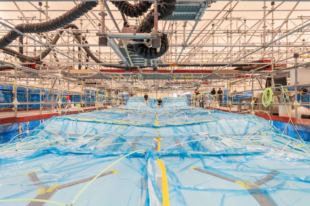 Interior of a Sunreef Yachts manufacturing facility with the hull of a yacht under construction, covered in protective blue material.